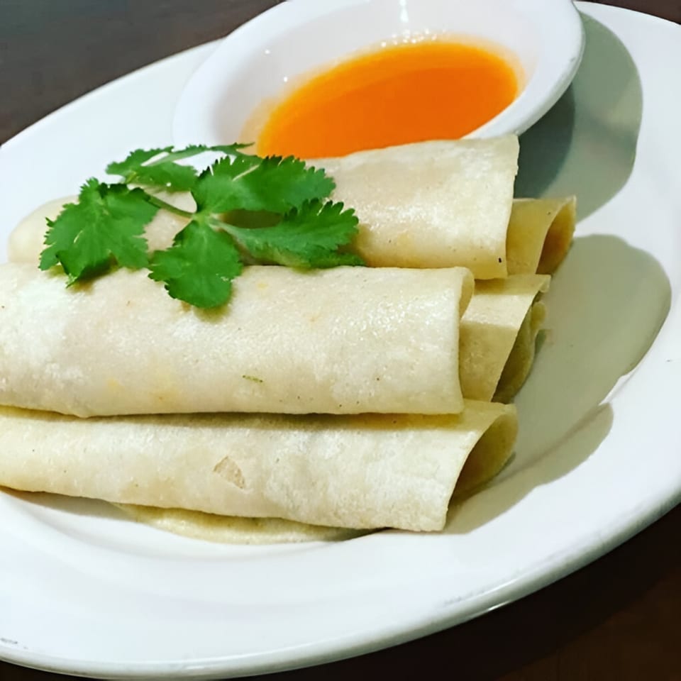 Belizean Caribbean spring rolls with cilantro garnish and a side of orange dipping sauce.